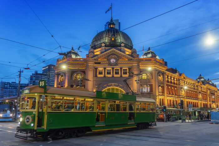 A tram passes Flinders Street Station at dusk.