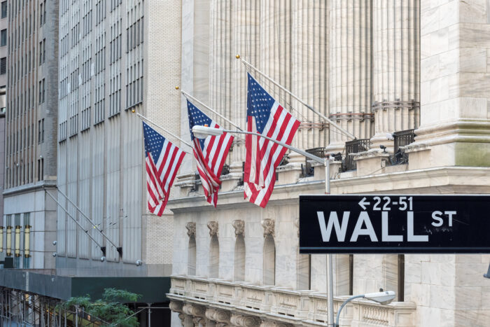 Wall Street sign with american flags and New York Stock Exchange in Manhattan, New York City, USA.