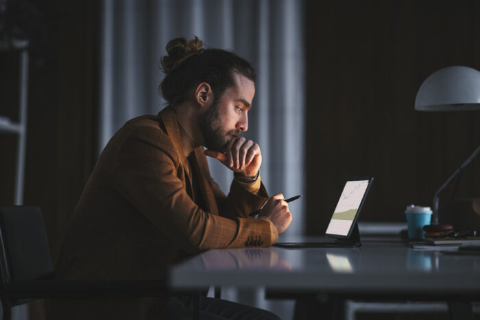 Thoughtful man looking at stocks investment on computer in the dark, considering what to do with inheritance