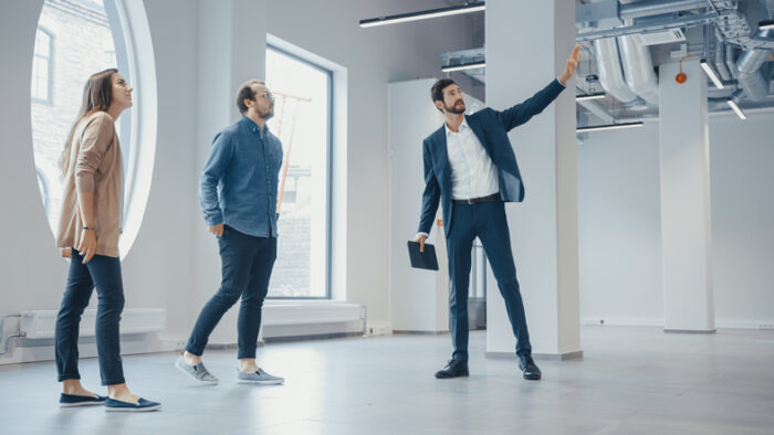 Real Estate Agent Showing a New Empty Office Space to Young Male and Female Hipsters. Entrepreneurs Meet the Broker with a Tablet and Discuss the Facility They Wish to Purchase or Rent.