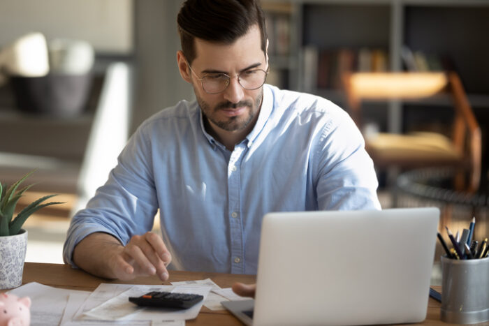 Focused young Caucasian man look at laptop screen calculate ebit for commercial property investment.