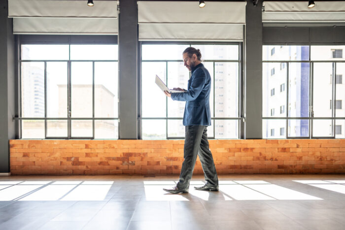 Mature businessman walking and using laptop at office to calculate EBIT of property