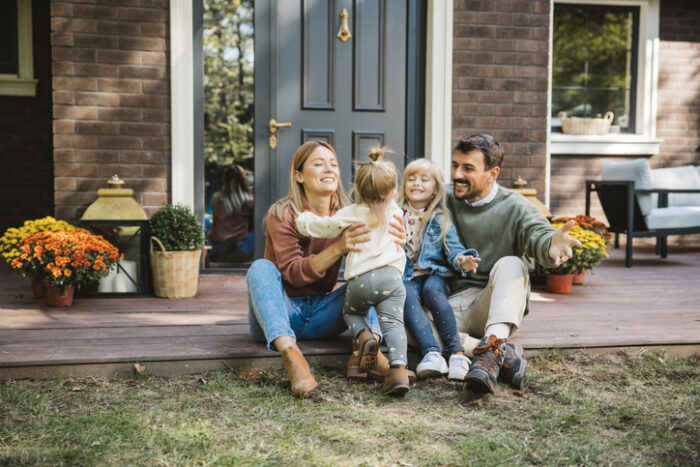 Young family with two kids having fun in front of there house. Porch is decorated with flowers.