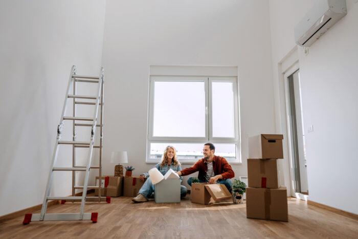 Young couple sitting on the floor at their new apartment, unpacking belongings after interest rate cut in February 2025.