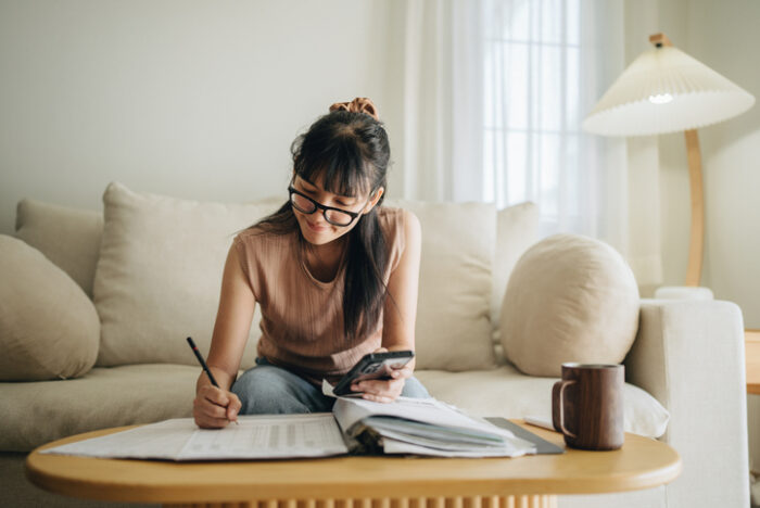 A woman sits at her living room with smartphone calculating negative gearing amount from her property investment in australia.