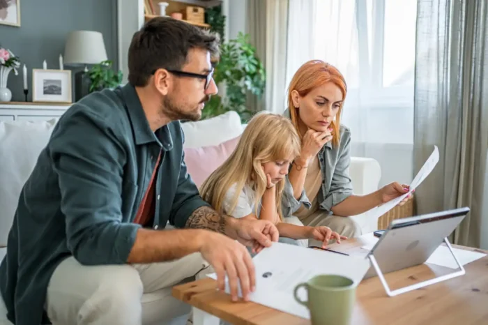 Family discussing whether to positively gear their Australian property on the couch with laptop and documents in front of them. 