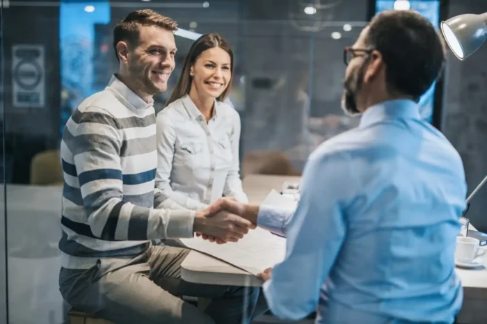 Young professional couple shaking hands with financial advisor in office. 