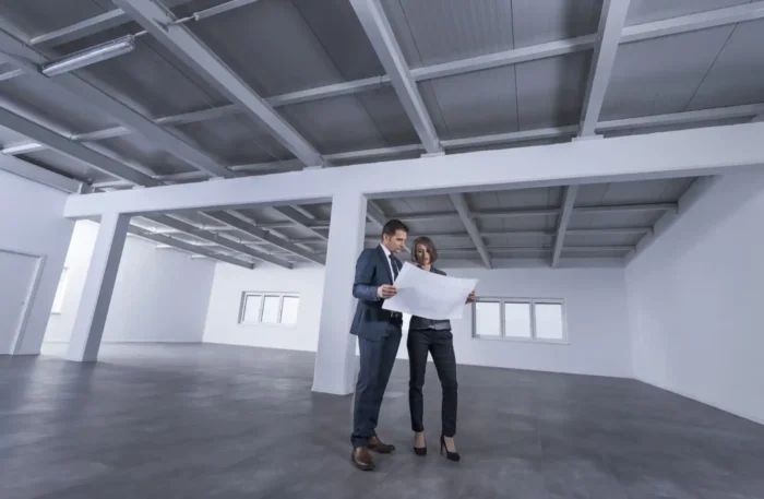 Two real estate landlords in commercial space looking at blueprint.