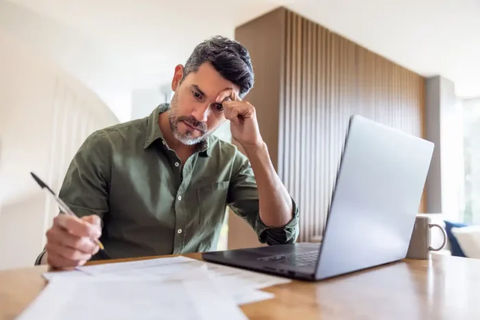 man stressed about buying average home in australia in his kitchen with laptop in front of him. 