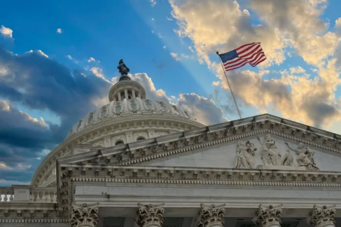 US White House from the ground up, with cloudy sky in background and US flag waving in the wind 